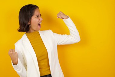 Çekici beyaz kadın zaferi kutluyor yumruklarıyla havaya yumruk atıyor ve stüdyo arka planında fotokopi aletiyle ışıldayan dişli bir gülümsemesi var..