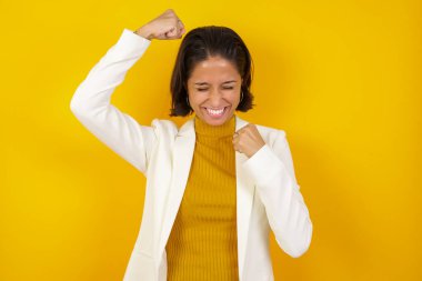 Çekici beyaz kadın zaferi kutluyor yumruklarıyla havaya yumruk atıyor ve stüdyo arka planında fotokopi aletiyle ışıldayan dişli bir gülümsemesi var.