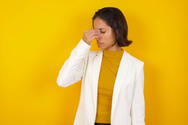 Çok üzgün, çekici, hoş bir iş kadını sarı arka planda duruyor gözlerinin arasına dokunuyor, ağlamak istiyor, stresli bir ilişki yaşıyor, yorgun, işle ilgili sorunlar yaşıyor.