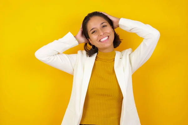 Confidence and coquettish concept. Portrait of charming young business girl, smiling broadly with self-assured expression while holding hands over her head. Standing against background