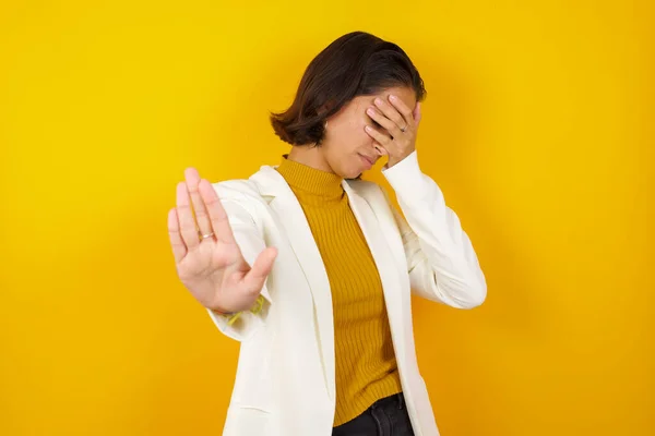 Young European woman covers eyes with palm and doing stop gesture, tries to hide from everybody. Don\'t look at me, I don\'t want to see, feels ashamed or scared.