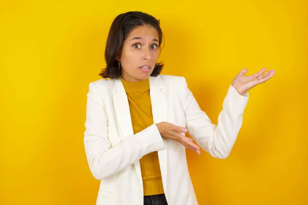 Beautiful European girl pointing aside with both hands showing something strange and saying: I don\'t know what is this. Standing against studio background. Advertisement concept.