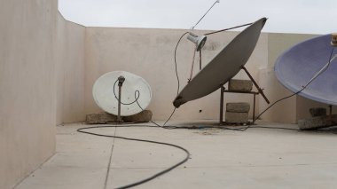 Çatıda sarmalanmış kablolu ve beton kaplamalı iki uydu anteni var..