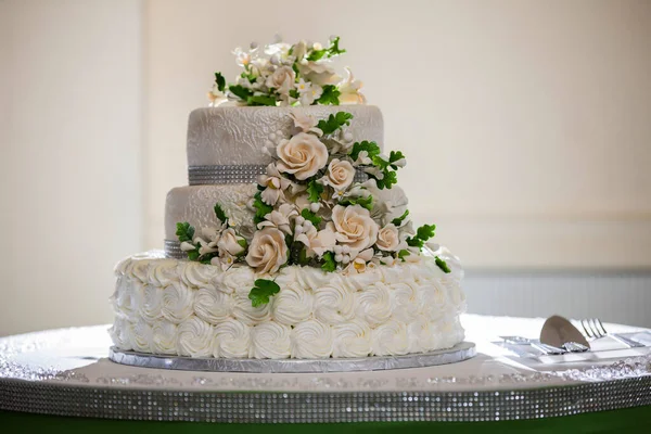 wedding cake close-up photo of a beautiful white three-tiered wedding cake decorated by flowers and greenery