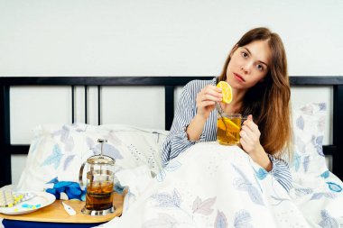 Bir fincan çayla yatakta tek başına oturan genç kadın