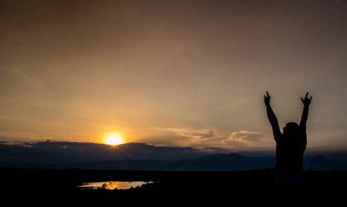 Adam gün batımında ayakta ve kolunu kaldırıyor.