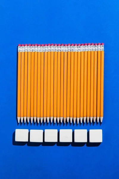 Pencils: pattern of orange pencils and white erasers from above on blue background. Office and school concept