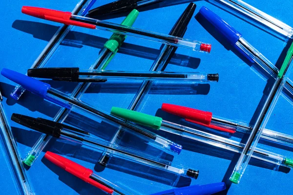 Pens: pattern of green, black blue and red colored pens from above on blue background. Office and school concept