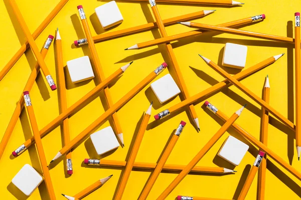 Pencils: pattern of orange pencils and white erasers from above on yellow background. Office and school concept