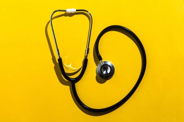 Sarı arka planda steteskop var. Tıbbi, koronavirüs, COVID-19 ve koruyucu kavram