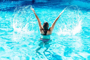 Havuzda sırtüstü uzanmış, kolları paradisial suda olan bir kadın.