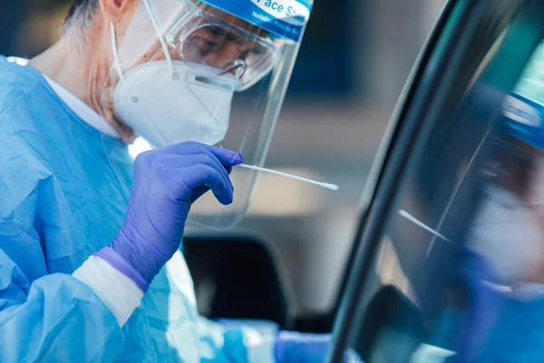 PPE takan tıbbi personel, ellerinde bir bezle PCR uyguluyor, arabasındaki bir hastaya COVID-19 bulaşmış mı diye bakıyor.