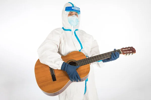 Doktor kadın koronavirüsle savaşmak için PPE giyiyor, gitar çalıyor, beyaz arka planda. Savaşçı. COVID tıp konsepti