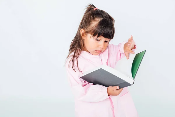 Brünettes Mädchen Mit Kinderschürze Die Auf Weißem Hintergrund Liest Schulkonzept — Stockfoto