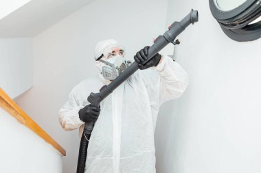 PPE giyen bir adam COVID 19 penceresinin yanındaki evi dezenfekte ediyor. Salgın sağlık konsepti