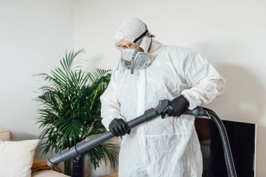 PPE giyen bir adam COVID-19 dezenfektan makinesiyle bir evin oturma odasını dezenfekte ediyor. Salgın sağlık konsepti