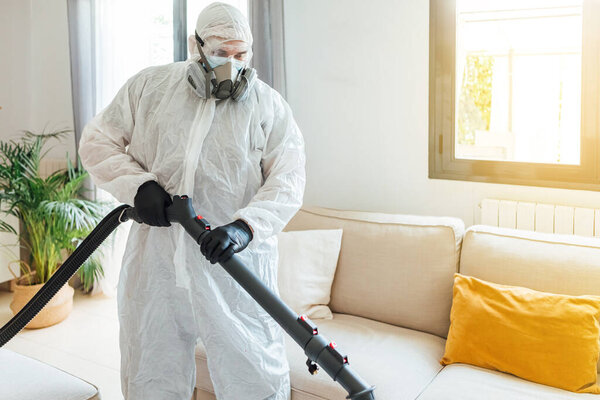 Man wearing PPE disinfecting the living room of a house with a COVID-19 disinfectant machine. Pandemic healthcare concept