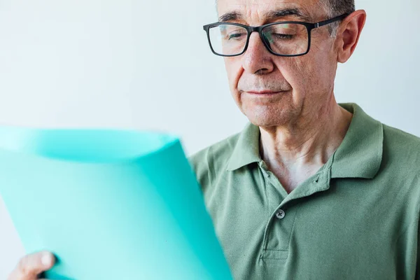 Entrepreneur retired man wearing a green polo shirt and glasses, holding a folder with a report