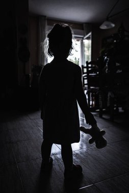 Küçük kız, korkunç bir duvarda bez bebeğiyle ışığa karşı duruyor. Cadılar Bayramı korku konsepti