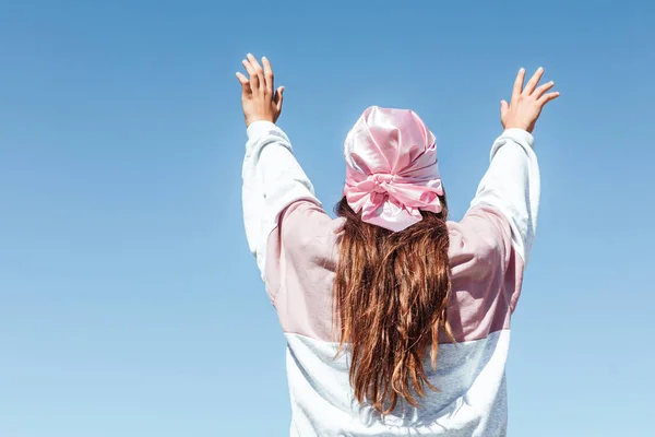Girl with her back turned with a pink headscarf,  on October 19,  International Breast Cancer Day, with the sky in the background. Breast cancer concept