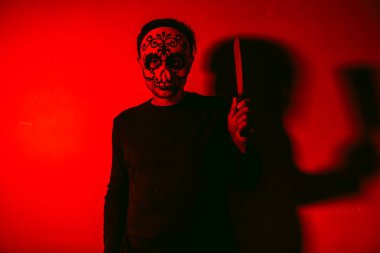 Cadılar Bayramı kafatası maskeli bir adam elinde kırmızı ışıkla et satırı tutmakla tehdit ediyor.