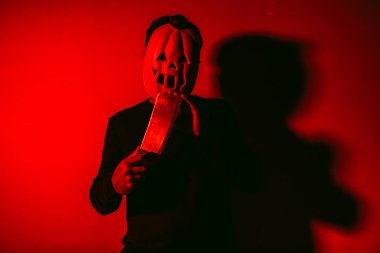 Cadılar Bayramı balkabağı maskeli bir adam kırmızı ışıklı et satırı tutuyor.