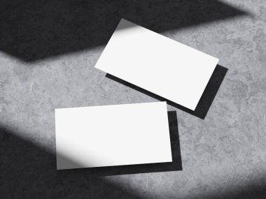 Çimento duvarındaki keskin ışığın altında iki kartvizit..