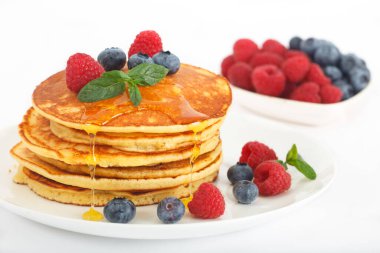 Ahşap tahtada taze pişmiş Amerikan gözlemesi yığını. Üstünde akçaağaç pekmezi, yabanmersini ve ahududu var. Rustik biçim resmi. 