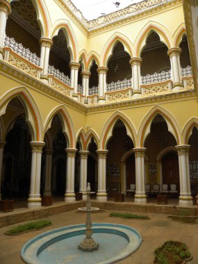 Sarı, bej, turuncu Maharanis avlusunda beyaz sütunlar, ızgaralar ve yeşil bitkiler Bangalore Sarayı 'nda çimenler