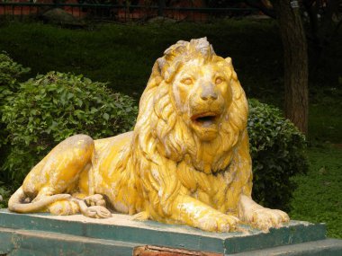 Cubbon Park 'taki sarı renkli aslan heykeli. Arka planda yeşil bitkiler ve ağaçlar var. 
