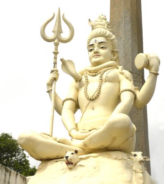 Shivagange 'da meditasyon pozisyonunda oturan Lord Shiva' nın sarı renkli taş heykeli. Arkasında koyu gri bulutlar var. 