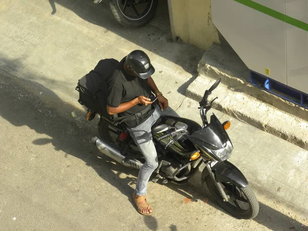 路上でバイクに座って携帯電話を確認するヘルメットを被った配達人 — ストック写真