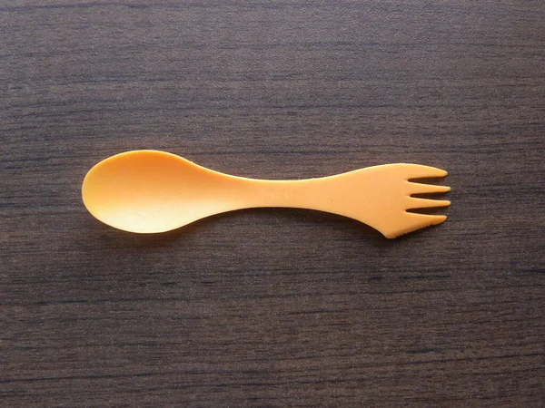Turuncu renk küçük plastik kaşık çatal ve bıçak kombinasyonu ahşap masada duruyor.