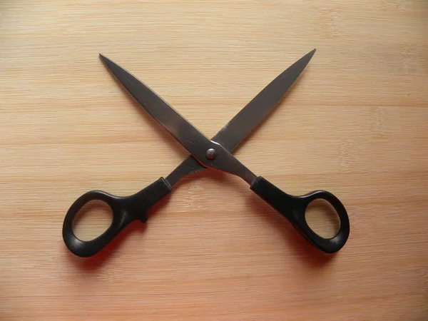 Open black color scissors on wood background