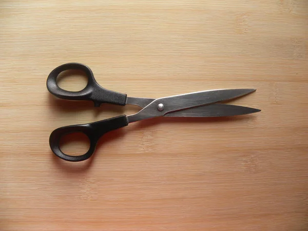 Open black scissors on wood background