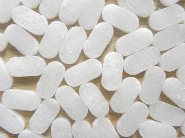 Beyaz renkli, dikdörtgen kafur tabletleri ahşap masada tutulur.