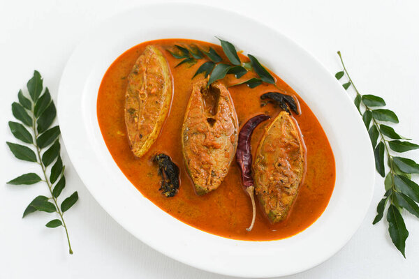 Top view of traditional Goan Pomfret or King fish curry Goa, India on white background. Hot and spicy homemade yellow fish curry made using coconut milk , gambooge, turmeric. 