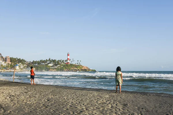 Kerala, Hindistan - 08 Eylül 2019: Kovalam plajı ve Vizhinjam deniz feneri. İnsanlar Trivandrum 'da deniz kıyısında eğleniyor..