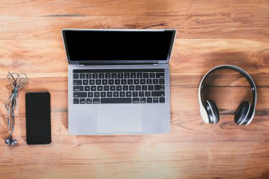 Üst manzara masası, dizüstü bilgisayarı, akıllı telefonu, kulaklığı ve kulaklığı olan ahşap müziği dinleyin.