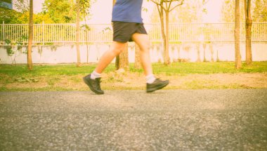 Hareket bulanıklığı yakın mesafe koşucusunun bacakları açık günbatımı arkaplanı ile sokakta koşar.