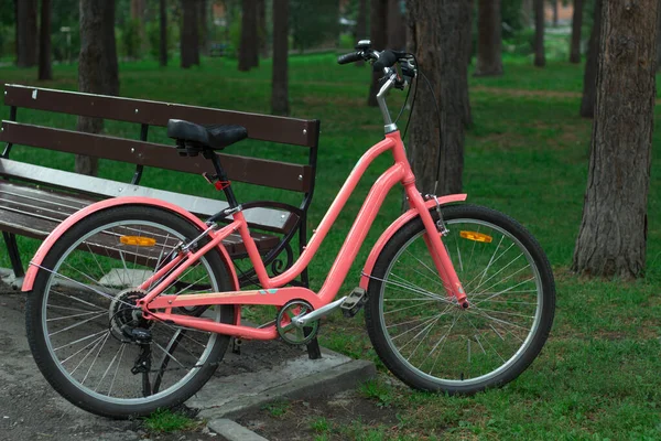 ベンチの近くの松公園でピンクの女性用シティバイク ストリート ライフスタイル サイクル — ストック写真