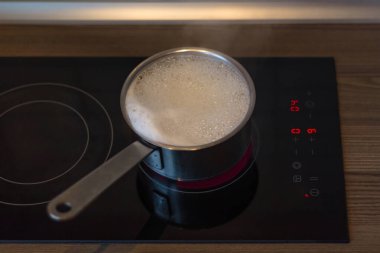 Seramik bir fayansta bir tencere kaynar su. Mutfak, yemek pişirme. Soba açık kalmış. Suda kabarcıklar.