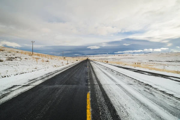 Idaho, Usa 'da bulutlu bir sabahta yarı karla kaplı uzun düz bir yol.