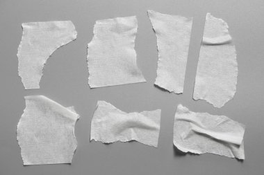 Gri arka plan üzerinde beyaz teyp kümesi. Yatay ve farklı boyut beyaz yapışkan bant, yapıştırıcı parçaları yırtılmış.