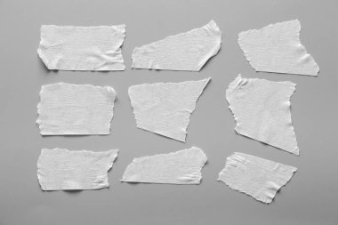 Gri arka plan üzerinde beyaz teyp kümesi. Yatay ve farklı boyut beyaz yapışkan bant, yapıştırıcı parçaları yırtılmış.