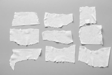 Gri arka plan üzerinde beyaz teyp kümesi. Yatay ve farklı boyut beyaz yapışkan bant, yapıştırıcı parçaları yırtılmış.