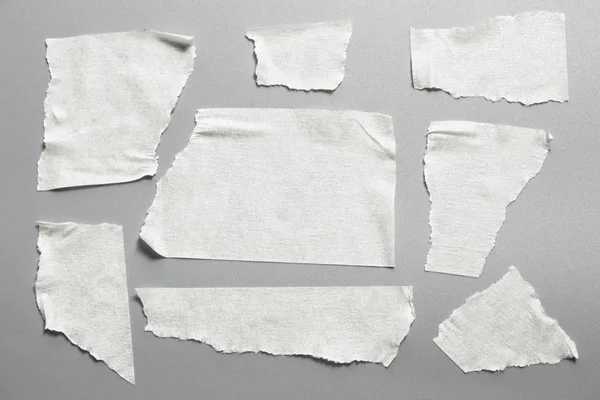 Gri arka plan üzerinde beyaz teyp kümesi. Yatay ve farklı boyut beyaz yapışkan bant, yapıştırıcı parçaları yırtılmış.