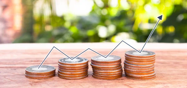 Tahta masa üzerinde dokunmatik madeni para ile yukarı aşağı çizgi grafikleri ve yeşil doğa arka planı, finans kavramı.
