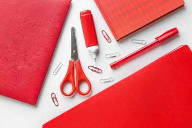 Office supplies in red and white colors: notepads, scissors, pen with cap, corrective pen and a lot of paper clips. Flat lay, top view clipart