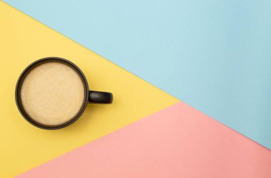 Kahve fincanı olan parlak bir poster. Sarı, pembe ve mavi üçgenlerin geometrik arkaplanı. Üst görünüm, kopyalama alanı ile